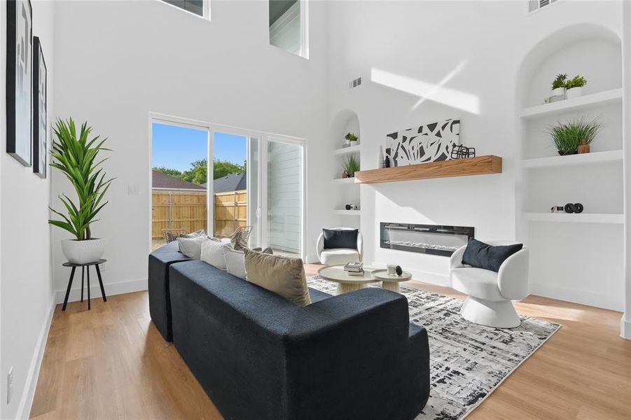 Living room with built in shelves, a glass covered fireplace, light wood finished floors, and a high ceiling