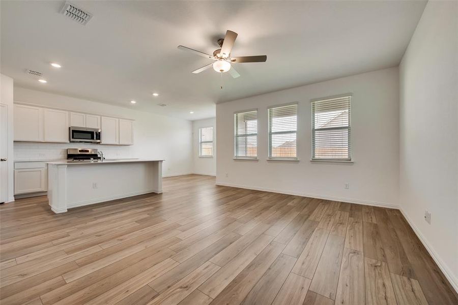 Kitchen featuring ceiling fan, stainless steel appliances, a center island with sink, light wood-type flooring, and white cabinetry