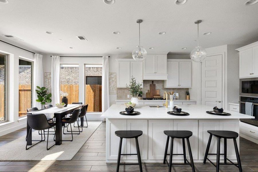 A well-lit kitchen with a spacious island, rich hardwood flooring, and abundant natural light streaming through large windows.