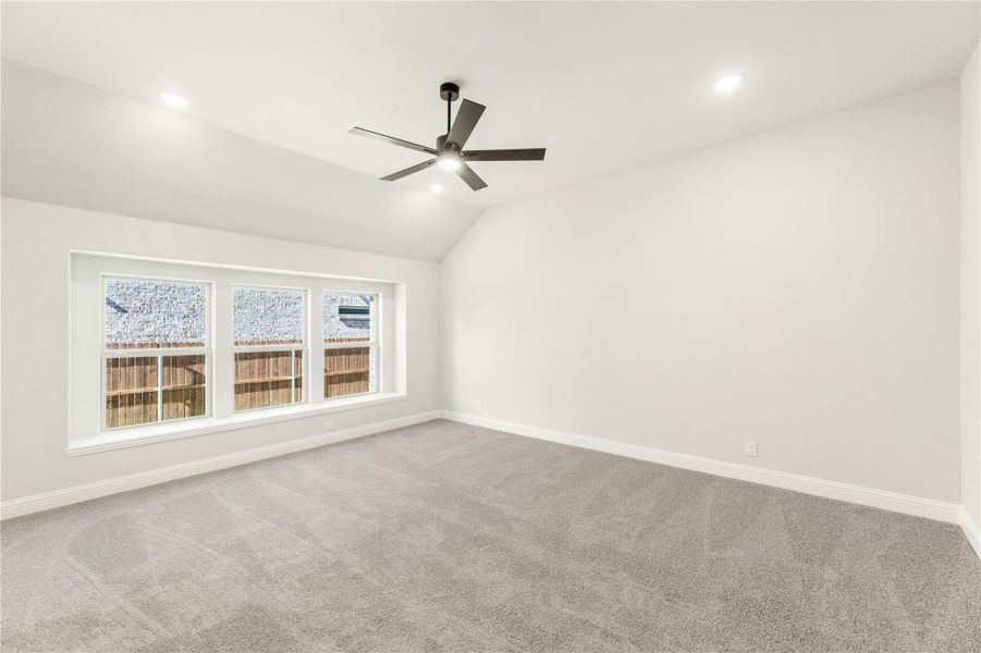 Empty bedroom with vaulted ceiling, ceiling fan, gray carpet, and triple window