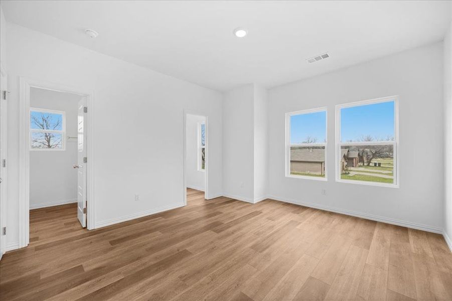 Spacious primary bedroom featuring wood-look flooring, neutral paint, and abundant natural light. Includes a private en-suite bathroom and walk-in closet.