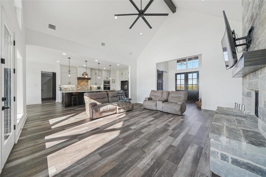 Living area with ceiling fan, dark wood-type flooring, a fireplace, french doors, and beam ceiling