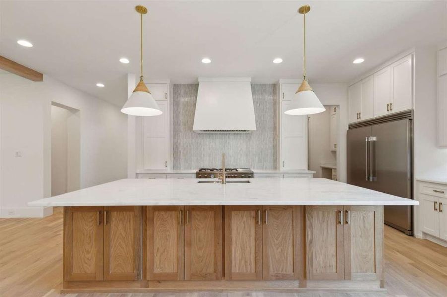 Kitchen featuring hanging light fixtures, a large island with sink, white cabinets, built in fridge, and custom exhaust hood