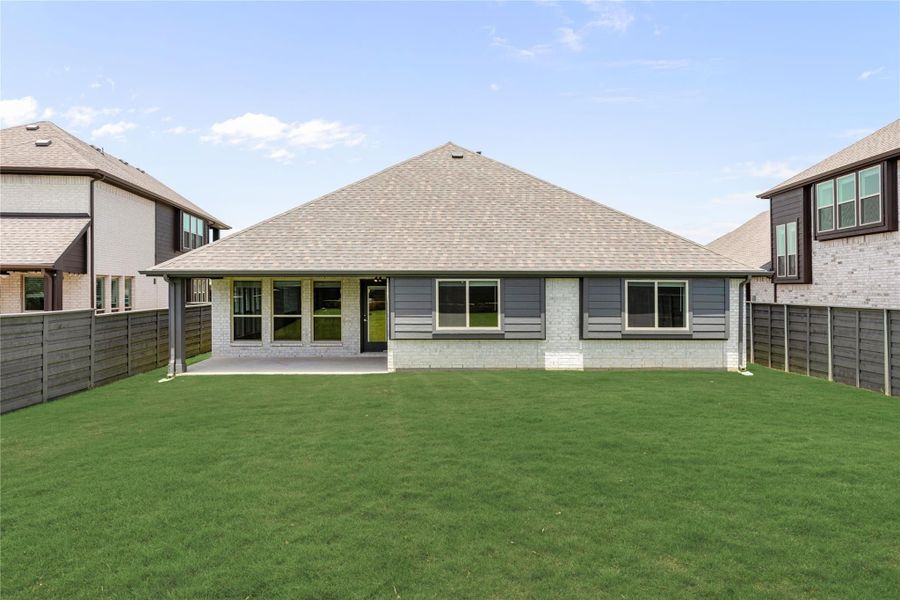 Rear exterior of single-story home with gray siding, brick accents, covered patio, and large fenced backyard Rear exterior of single-story home with gray siding, brick accents, covered patio, and large fenced backyard