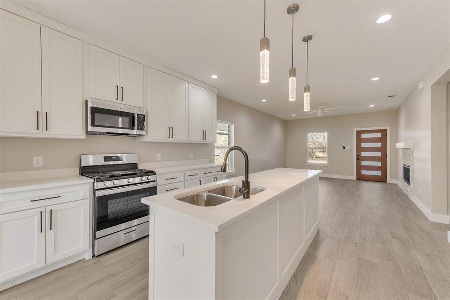 Kitchen with sink, white cabinetry, decorative light fixtures, appliances with stainless steel finishes, and a kitchen island with sink