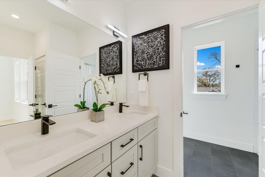 Spa-inspired luxury. This bathroom features a double vanity with crisp quartz countertops, matte black hardware, and a contemporary LED light fixture.