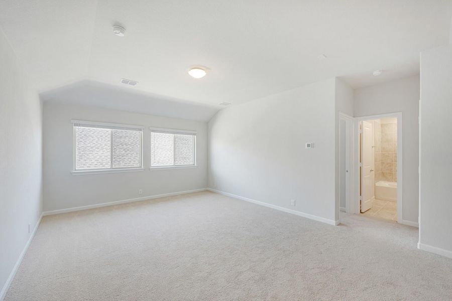 Empty master bedroom with vaulted ceiling, carpet flooring, and ensuite bathroom doorway visible