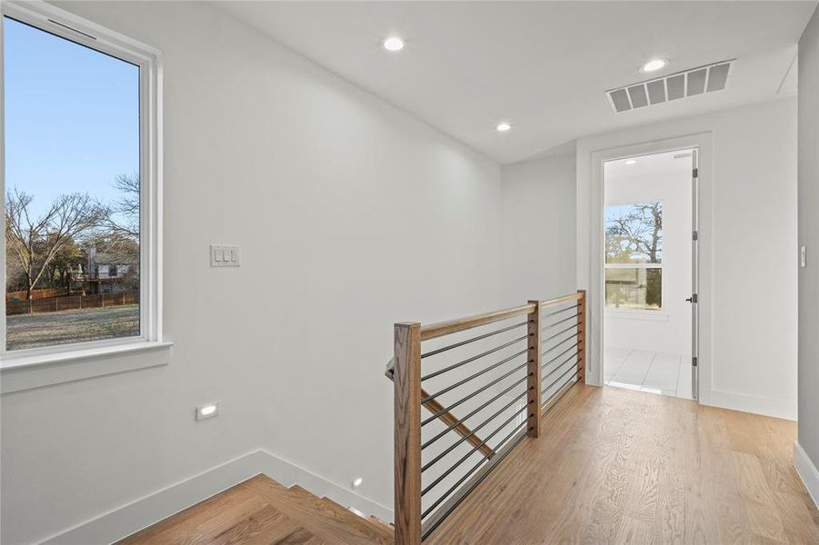 Hall with light wood-type flooring, baseboards, visible vents, and an upstairs landing