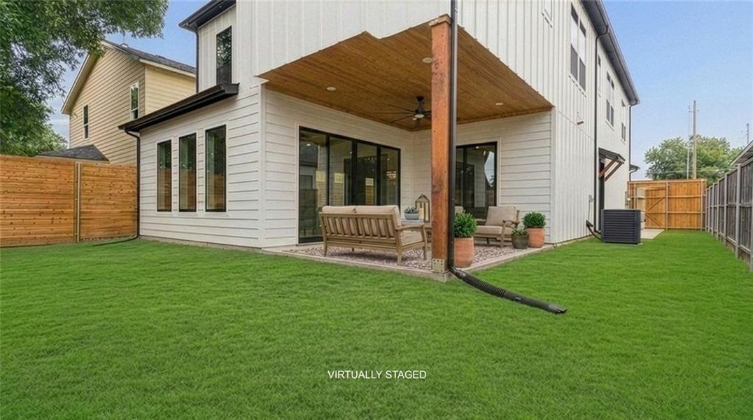 Expansive rear yard featuring a covered patio with a wood-finish ceiling and a ceiling fan, a concrete patio surface, a broad lawn, and vertical wooden fencing Expansive rear yard featuring a covered patio with a wood-finish ceiling and a ceiling fan, a concrete patio surface, a broad lawn, and vertical wooden fencing