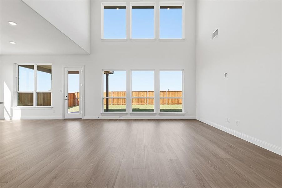 Unfurnished living room featuring light wood finished floors, a high ceiling, and recessed lighting Unfurnished living room featuring light wood finished floors, a high ceiling, and recessed lighting