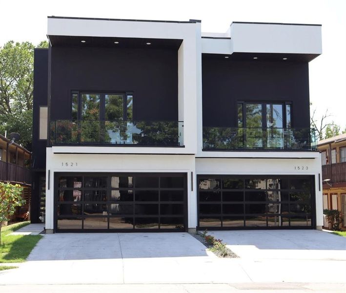 Front view of house with driveway, attached garage with glass door, and stucco siding.