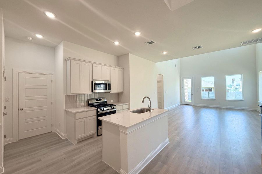 Open-concept living space featuring a kitchen island with sink, stainless steel appliances, light wood-finish flooring, recessed lighting, and multiple windows Open-concept living space featuring a kitchen island with sink, stainless steel appliances, light wood-finish flooring, recessed lighting, and multiple windows