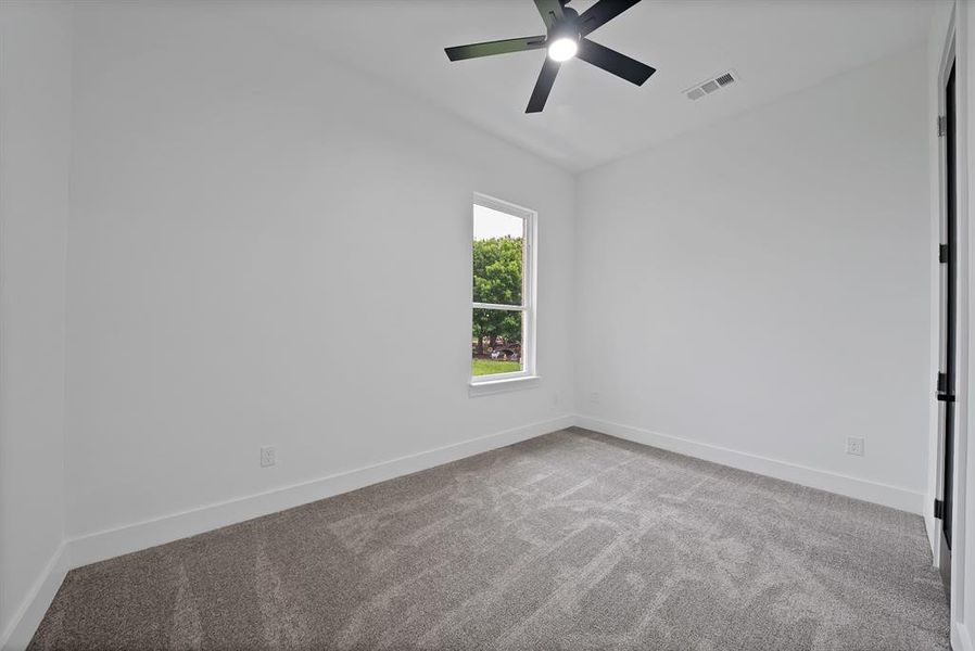 This room offers neutral colored walls and carpet, a modern ceiling fan, and a window providing natural light