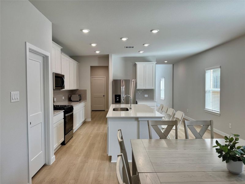 Modern open-concept kitchen and dining area. It features light wood flooring, white cabinetry, and stainless steel appliances. The space is bright with natural light from multiple windows, offering a welcoming atmosphere. Modern open-concept kitchen and dining area. It features light wood flooring, white cabinetry, and stainless steel appliances. The space is bright with natural light from multiple windows, offering a welcoming atmosphere.