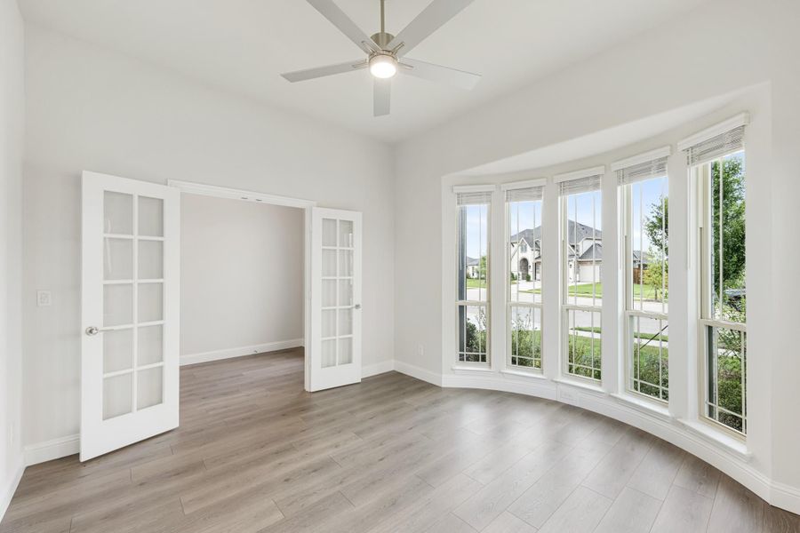 Empty room with hardwood floors, bay windows, French doors, and ceiling fan Empty room with hardwood floors, bay windows, French doors, and ceiling fan