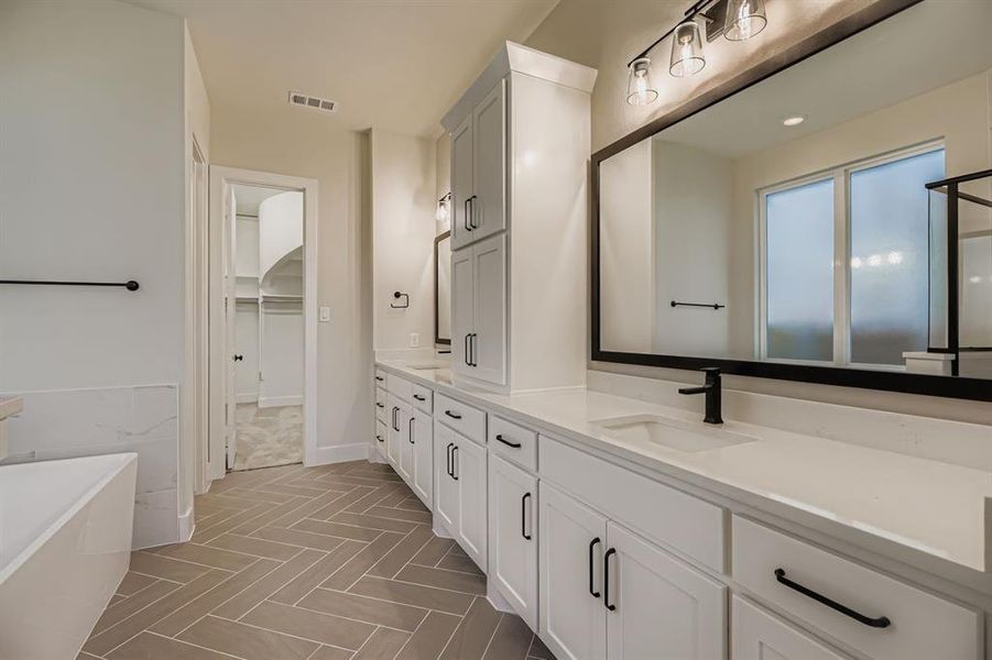 Bathroom featuring double vanity, a spacious closet, and a tub to relax in