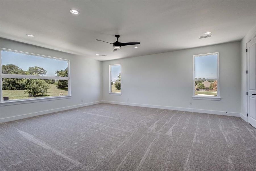 Spacious room featuring neutral carpeting, a contemporary ceiling fan, and multiple windows
