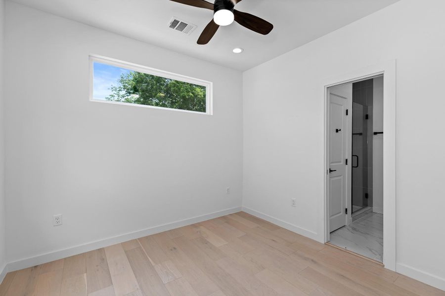 Blonde wood flooring extends through this naturally illuminated room, leading to a chic adjoining bathroom.