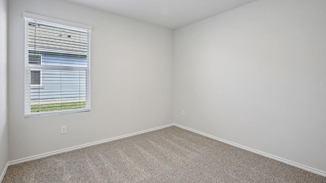 A well-lit bedroom with pristine carpeting and a window overlooking lush green space.