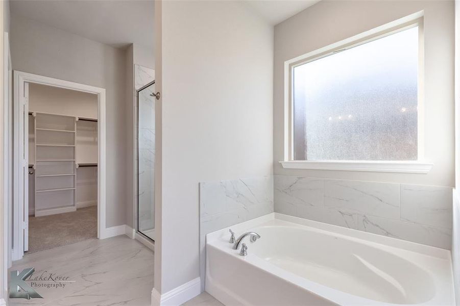 Bathroom featuring a walk in closet, a bath, light marble finish flooring, and a stall shower