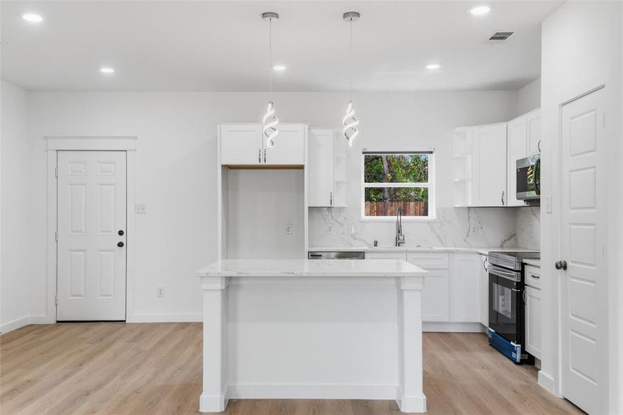 Modern kitchen featuring a central island with a light-toned countertop, white cabinetry, integrated sink, and an electric range
