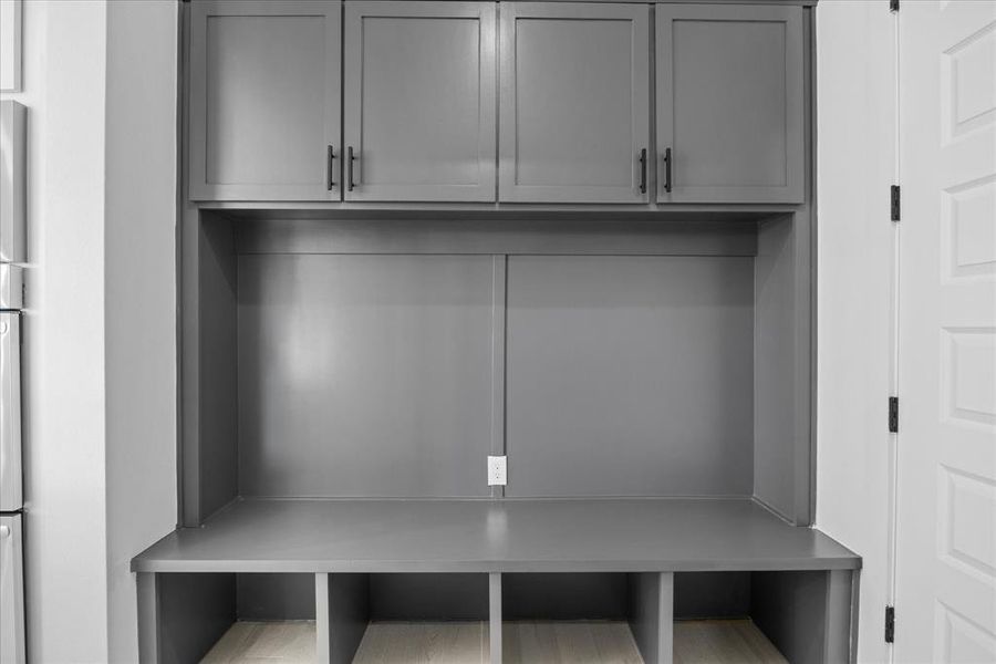 Built-in mudroom station featuring grey shaker-style cabinetry with matte black hardware, integrated bench seating, and open storage cubbies below