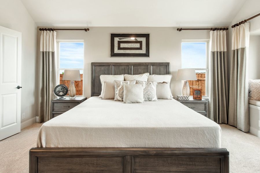 Bedroom with king-size bed, dark wood headboard, two nightstands, and large windows with gray curtains