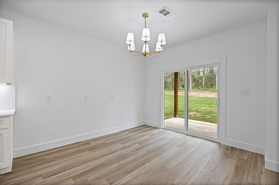 Spacious room featuring wood-finish flooring, white baseboards, and a modern chandelier Spacious room featuring wood-finish flooring, white baseboards, and a modern chandelier