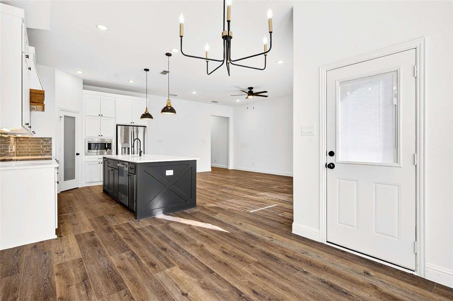 Kitchen featuring a chandelier, white cabinets, tasteful backsplash, pendant lighting, and an island with sink