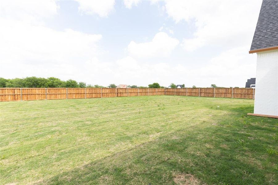 Expansive backyard featuring a large grass area, full privacy fencing, and a side exterior wall with white brick and dark shingles