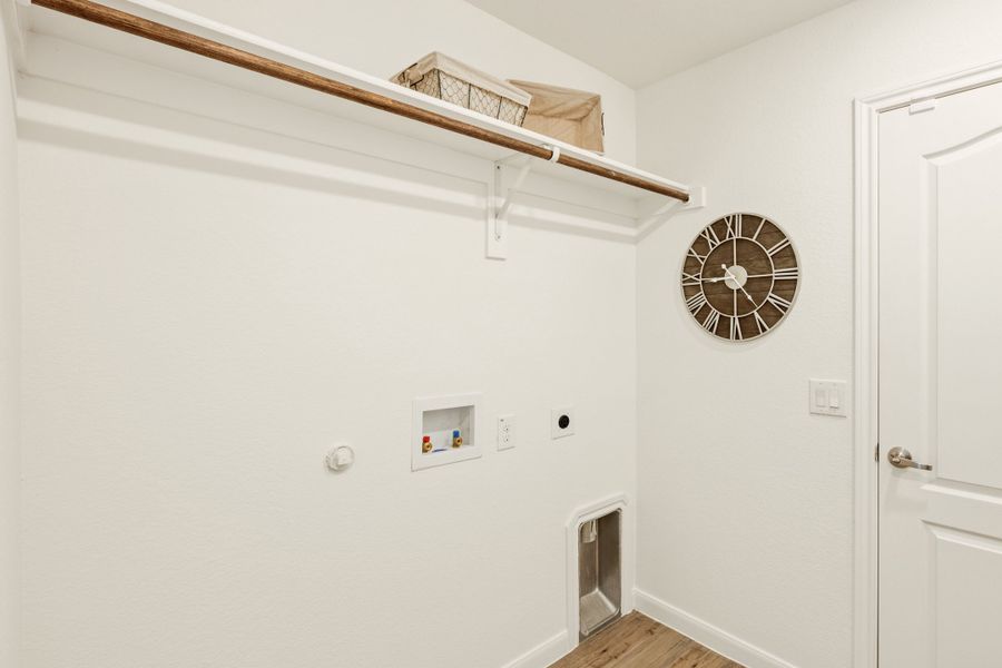 Laundry room with wood hanging rod, upper shelf, washer hookups, and decorative wall clock