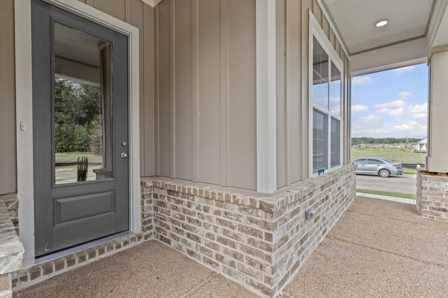 Property entrance featuring board and batten siding, a porch, and brick siding