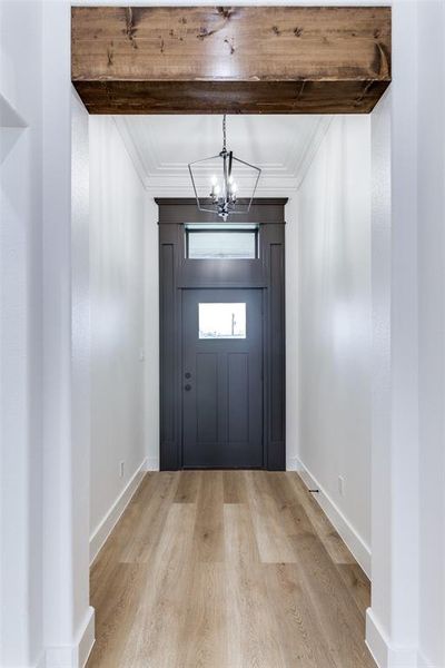 Foyer with an inviting chandelier, light wood-style flooring, ornamental molding, and baseboards