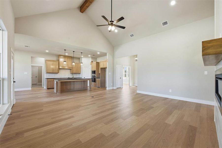 Unfurnished living room featuring a glass covered fireplace, high vaulted ceiling, light wood-style floors, beam ceiling, and recessed lighting