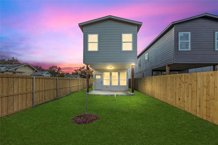 Back house at dusk featuring a lawn and a patio area