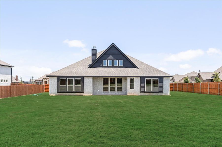 Rear view of single-story brick home with dark trim, large windows, and fenced backyard with green lawn