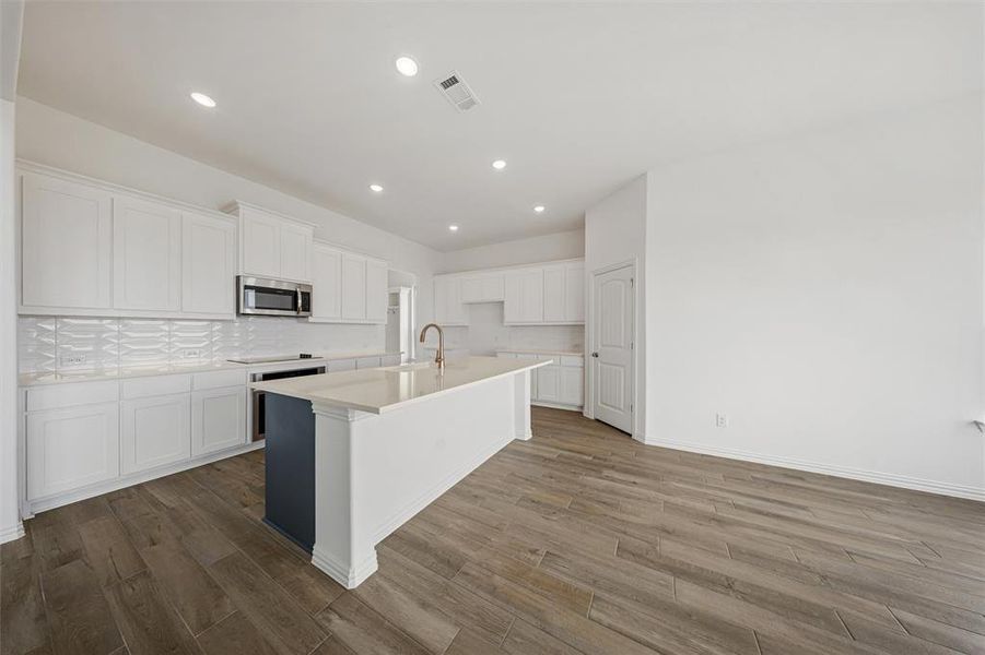 Kitchen featuring white cabinets, backsplash, a center island with sink, recessed lighting, and dark wood-style flooring Kitchen featuring white cabinets, backsplash, a center island with sink, recessed lighting, and dark wood-style flooring
