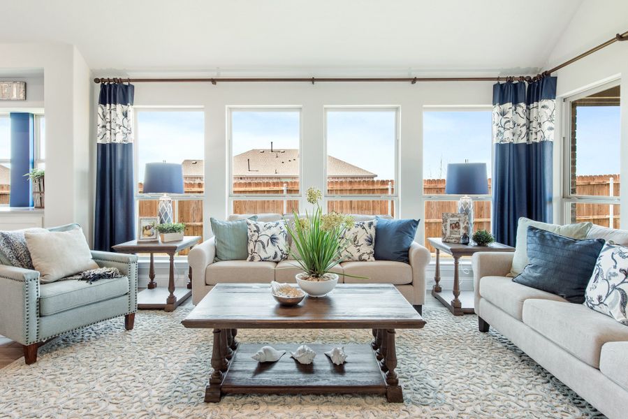 Living room with beige sofas, blue accent pillows, wood coffee table, and large windows with navy curtains