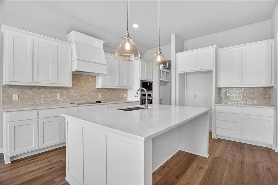 Kitchen featuring a large central island with a sink, white cabinetry, integrated stainless steel appliances, and wood-finish flooring Kitchen featuring a large central island with a sink, white cabinetry, integrated stainless steel appliances, and wood-finish flooring