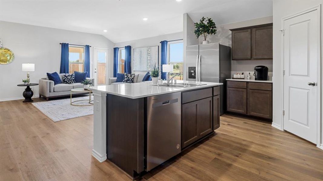 Kitchen featuring dark wood finish cabinetry, open floor plan, dishwasher, vaulted ceiling, and dark wood-type flooring