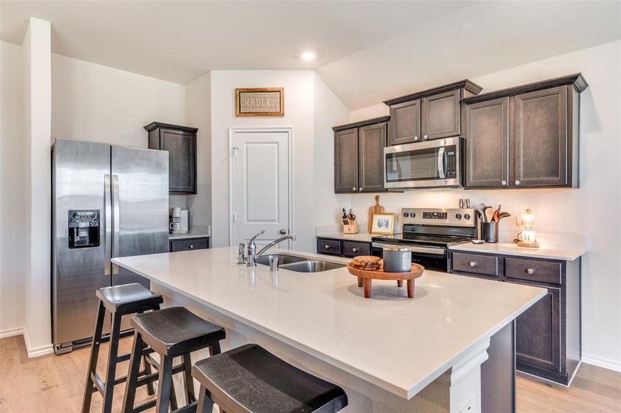 Kitchen with light wood-style floors, dark brown cabinets, stainless steel appliances, a breakfast bar, and recessed lighting