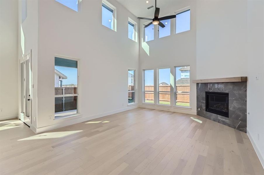 Unfurnished living room featuring light hardwood / wood-style floors, a fireplace, a wealth of natural light, and a high ceiling