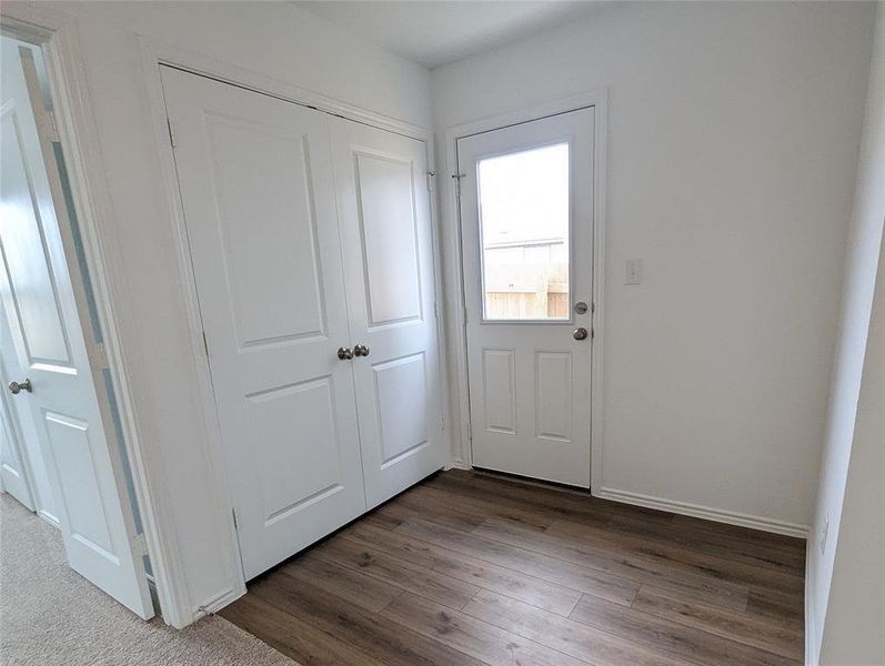 Hardwood-style flooring extends from the exterior door, complemented by crisp white trim and a closet.