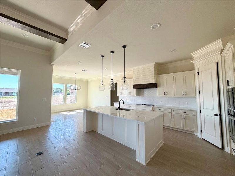 Kitchen featuring ornamental molding, a kitchen island with sink, white cabinetry, light stone countertops, and tasteful backsplash Kitchen featuring ornamental molding, a kitchen island with sink, white cabinetry, light stone countertops, and tasteful backsplash