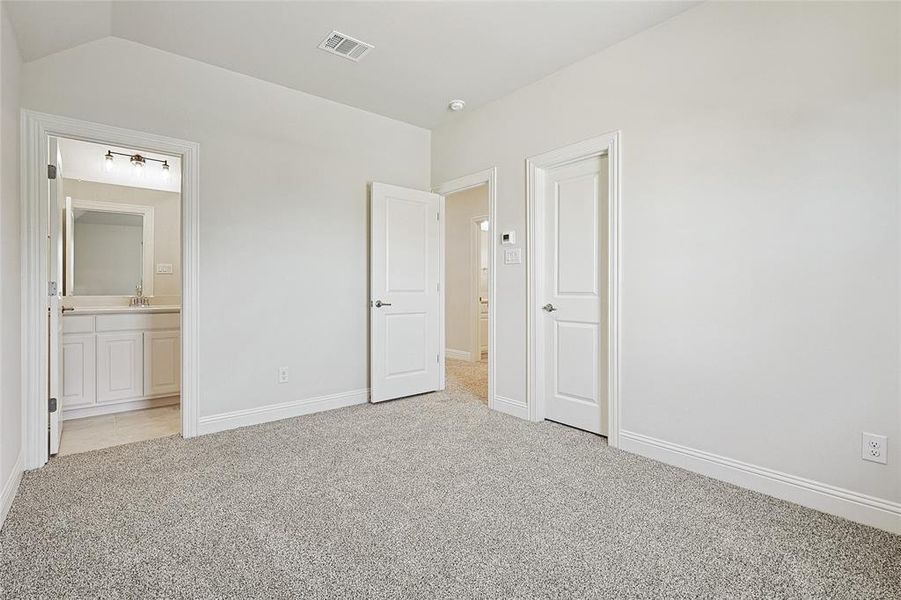 Unfurnished bedroom with connected bathroom, light colored carpet, and lofted ceiling