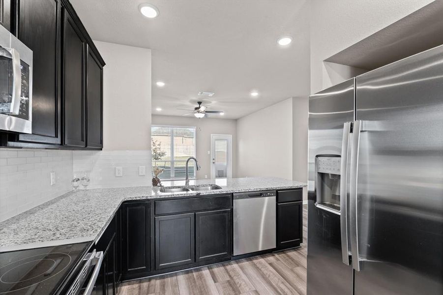 Kitchen with dark cabinetry, appliances with stainless steel finishes, light stone countertops, light wood-style flooring, and recessed lighting Kitchen with dark cabinetry, appliances with stainless steel finishes, light stone countertops, light wood-style flooring, and recessed lighting