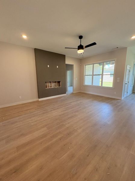 Recessed lighting, wood-finish flooring, ceiling fan with integrated light, large window with grid pattern, and a built-in media wall with open shelving Recessed lighting, wood-finish flooring, ceiling fan with integrated light, large window with grid pattern, and a built-in media wall with open shelving