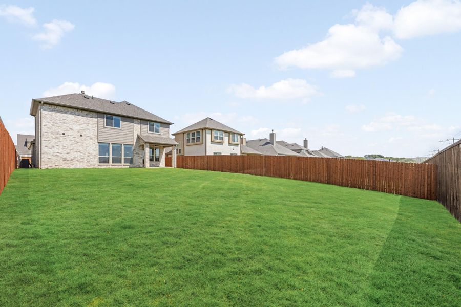 Backyard with large green lawn, wood privacy fence, and two-story stone and siding home exterior.