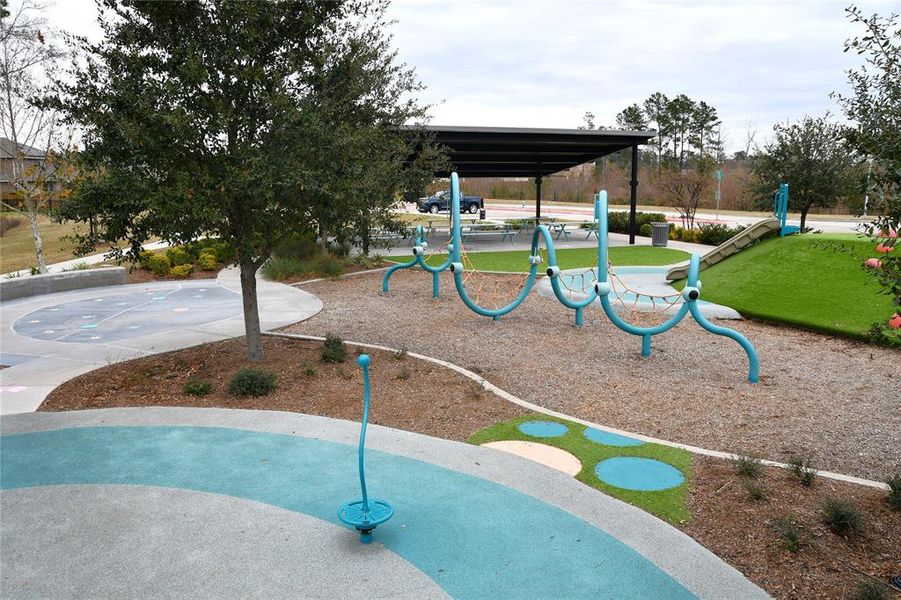 This photo showcases a modern, well-maintained community playground. It features unique climbing structures, a covered picnic area, and a small slide, set amidst landscaped greenery, perfect for family activities.