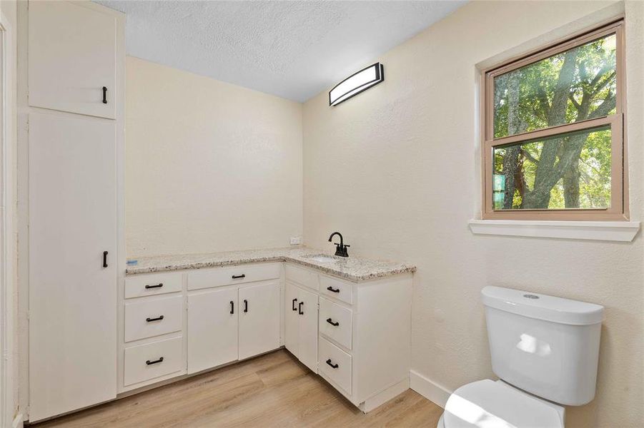 Half bathroom featuring vanity, light wood-style flooring, and a textured ceiling Half bathroom featuring vanity, light wood-style flooring, and a textured ceiling